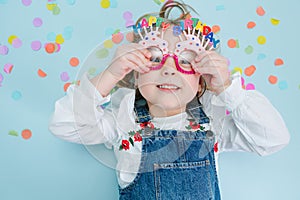 Happy little girl lies on a floor, holding onto her birthday glasses