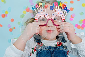 Happy little girl lies on a floor, holding onto her birthday glasses