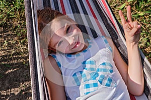 A happy little girl lies in a hammock in the garden in the summer. A child in a hammock during the holidays smiles in