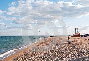 Happy little girl with long blond hair on seascape background blue cloudy sky. Child walking alone running on sand beach