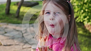 happy little girl with long blonde hair eating hot dog on outside