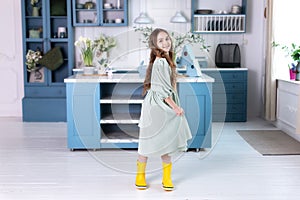 Happy little girl with long hair in dress and in yellow rubber boots spinning at room.