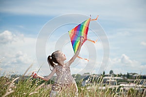 Happy little girl with long hair holding kite in the field on summer sunny day
