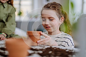 Happy little girl looking at growing plant in a pot.