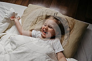 Happy little girl lying in bed smiling and laughing