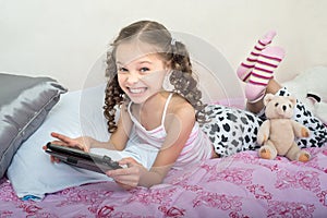 Happy little girl lying on bed with tablet computer