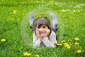 Happy little girl lying down on the grass with hands holding her face