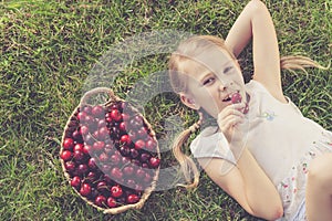 Happy little girl lying near the tree with a basket of cherries