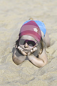Happy little girl lying on the sand on the beach