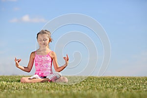 Happy little girl meditates on green field at