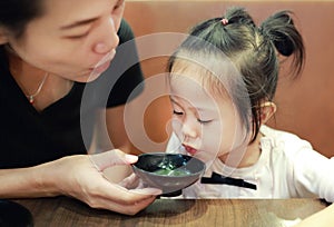 Happy little girl and mother blowing hot miso soup at japanese restaurant