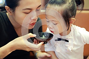 Happy little girl and mother blowing hot miso soup at japanese restaurant