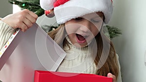 Happy little girl opens Christmas gift on background of Christmas Tree close up