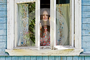 Happy little girl opens a window of rustic house in the early sunny morning