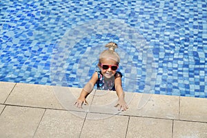 Happy little girl in outdoor swimming pool on hot summer day. Kids learn to swim. Children play in tropical resort. Family beach