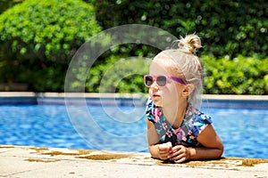 Happy little girl in outdoor swimming pool on hot summer day. Kids learn to swim. Children play in tropical resort. Family beach photo