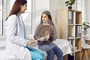 Happy little girl patient sitting on medical bed and talking to woman pediatrician