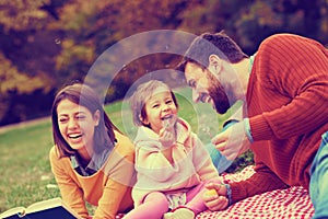 Happy little girl on picnic with her parents blowing dandelions