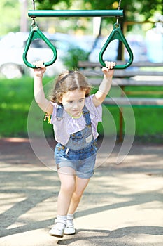 Happy little girl with pigtails hangs on the rings