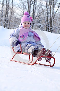 Happy little girl in pink scarf and hat goes tobogganing photo