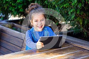 Happy Little girl play in tablet outdoors. Working Outside with