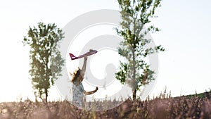 Happy little girl playing with airplane on a lavender field during sunset. Children play toy airplane. Little girl wants