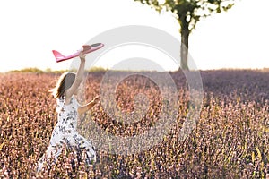 Happy little girl playing with airplane on a lavender field during sunset. Children play toy airplane. Little girl wants