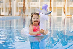 Happy little girl playing with colorful inflatable ring in outdoor swimming pool on hot summer day.