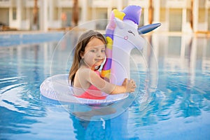 Happy little girl playing with colorful inflatable ring in outdoor swimming pool on hot summer day.