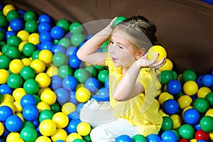 Happy little girl playing at colorful plastic balls playground