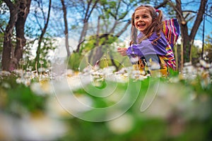 Happy little girl playing in the grass with flowers after the rain. She wear raincoat and yellow boots