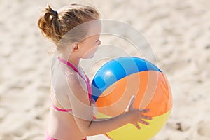 Happy little girl playing inflatable ball on beach