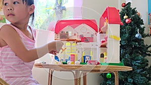 Happy little girl playing with plastic doll house with mini furniture toys and doll. Cute little girl in a pink dress enjoys in th