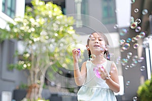 Happy little girl playing soap bubbles in garden