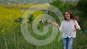 Happy little girl playing among soap bubbles on green meadow in summer