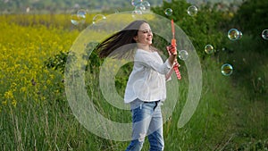 Happy little girl playing among soap bubbles on green meadow in summer