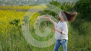 Happy little girl playing among soap bubbles on green meadow in summer