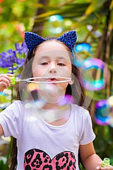 Happy little girl playing with soap bubbles on a summer nature, wearing a blue ears tiger accessories over her head in a