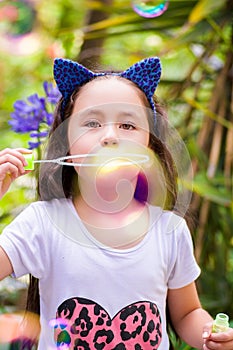 Happy little girl playing with soap bubbles on a summer nature, wearing a blue ears tiger accessories over her head in a