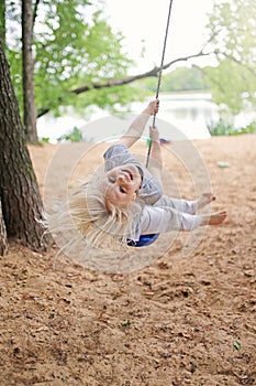 Happy Little Girl Playing on Swing on Beach by Lake