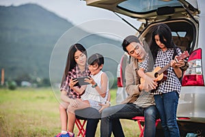 Happy little girl playing ukulele with asian family sitting in the car for enjoying road trip and summer vacation