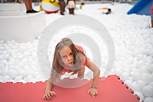 Happy little girl playing white plastic balls pool in amusement park