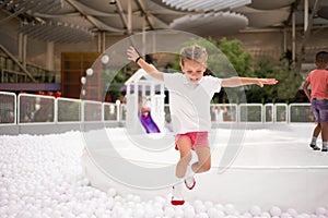 Happy little girl playing white plastic balls pool in amusement park. playground for kids
