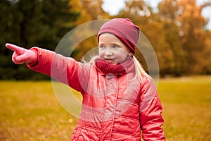 Happy little girl pointing finger in autumn park