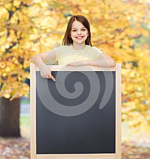 Happy little girl pointing finger to blackboard