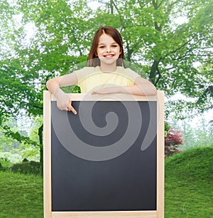 Happy little girl pointing finger to blackboard