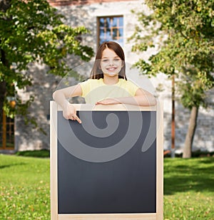 Happy little girl pointing finger to blackboard