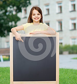 Happy little girl pointing finger to blackboard