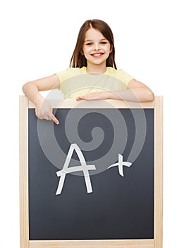 Happy little girl pointing finger to blackboard