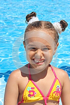 Happy little girl in the pool. Smiling baby girl in a swimming suit and with a funny hairstyle